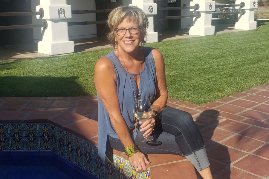 Jill Tweedie, Founder of Breakaway Tours seated on a Mexican style fountain holding a glass of white wine