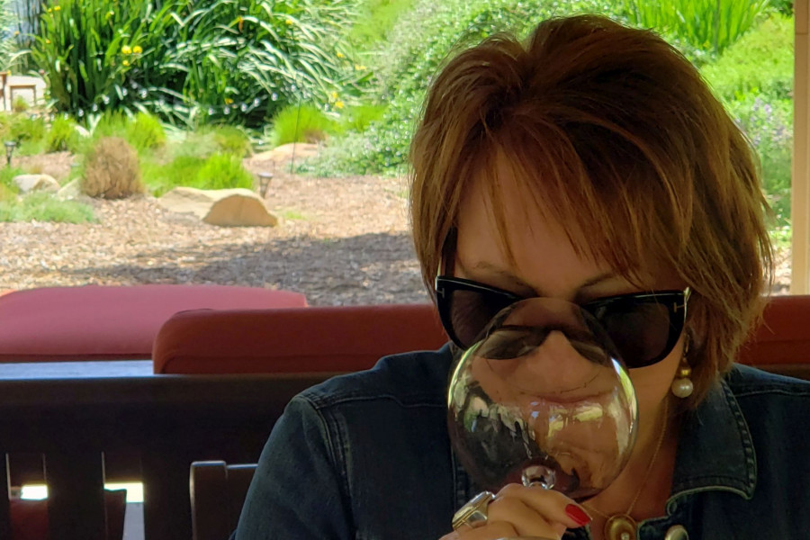 up close shot of woman wearing sunglass, smelling pinot noir in an outdoor setting